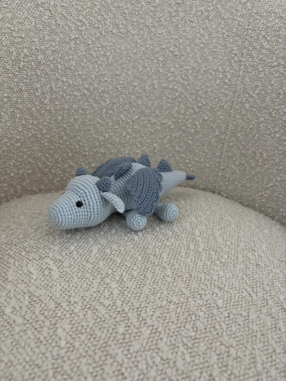A small crocheted blue dragon toy sitting on a chair